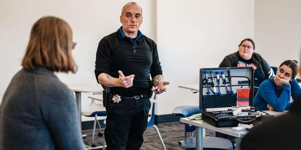 Social Science, Humanities, and Interdisciplinary Programs 1 A man in a black uniform with a badge stands and speaks to a small college group in a classroom. A case with various tools is open on the table beside him, while students from Maine listen attentively, eager to pursue their degree. Saint Joseph's College of Maine