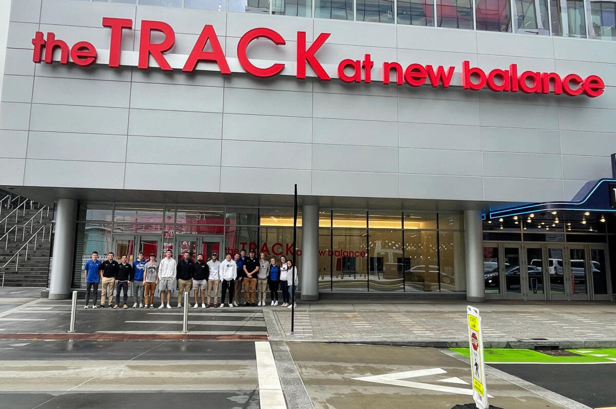Sport and Exercise Science Programs 5 A group of people stands in front of a building with the sign "the TRACK at new balance." The building exterior is modern with glass windows, showcasing a space that complements sport and exercise science programs. Saint Joseph's College of Maine