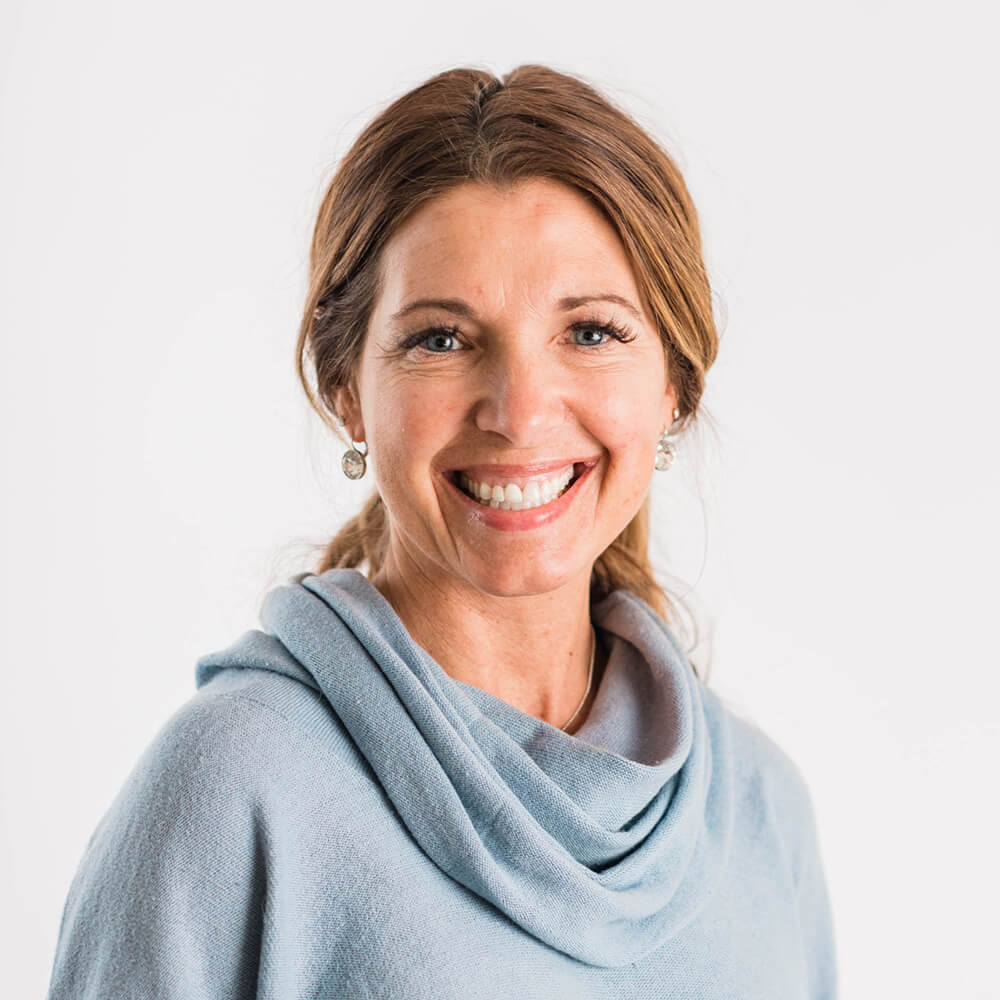 Rhonda-Mynahan_Oct2019_001_HR_sq Woman with long brown hair smiling, wearing a light blue sweater, and standing against a white background. Saint Joseph's College of Maine