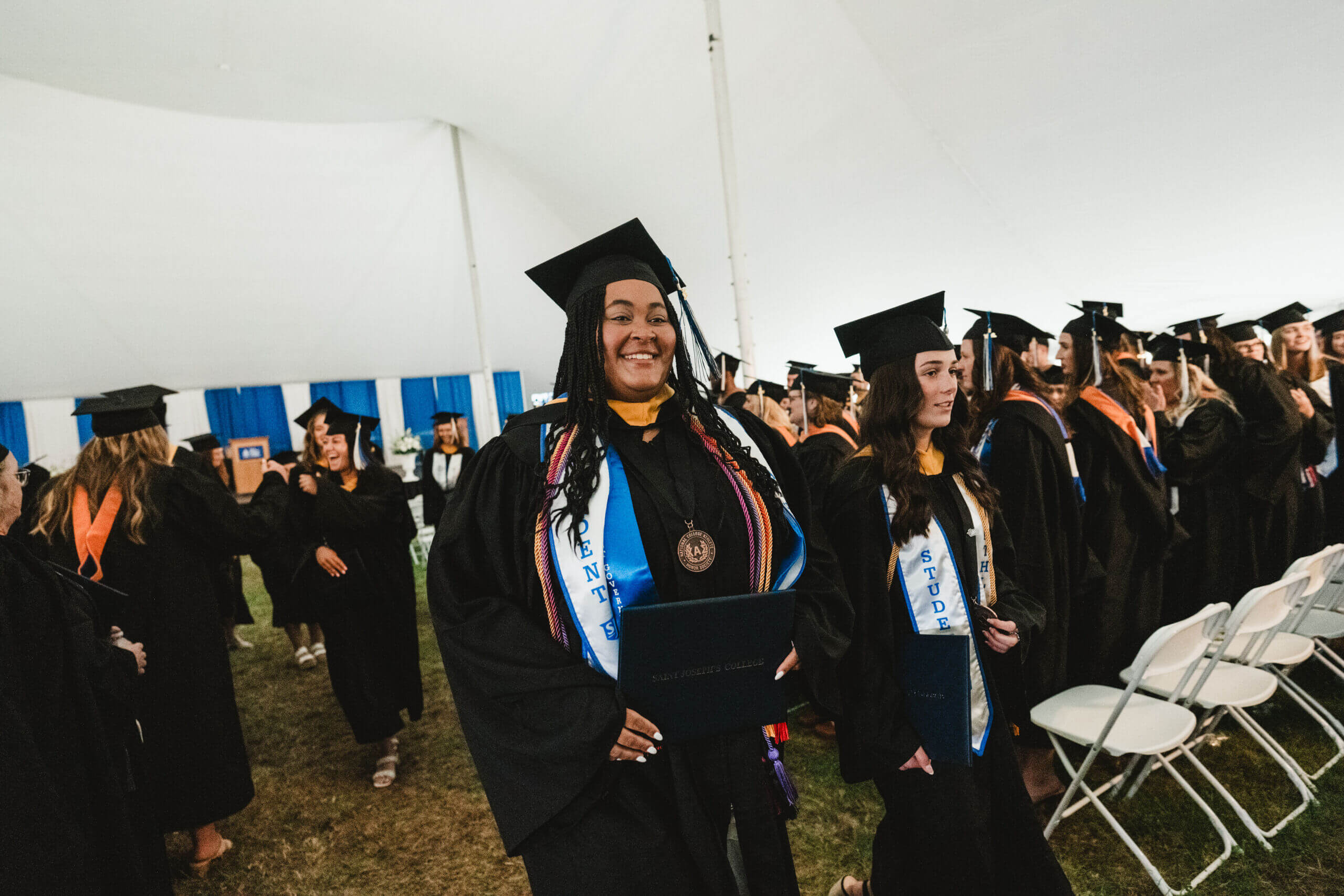 Commencement 7 Graduates in caps and gowns beam with pride, holding their diplomas inside the tent during the commencement ceremony. Saint Joseph's College of Maine