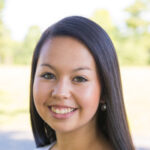 Samantha-Sim-2 A woman with long dark hair and a light complexion is smiling at the camera, showcasing the vibrant atmosphere of Saint Joseph's College of Maine campus in the blurred outdoor background. Saint Joseph's College of Maine
