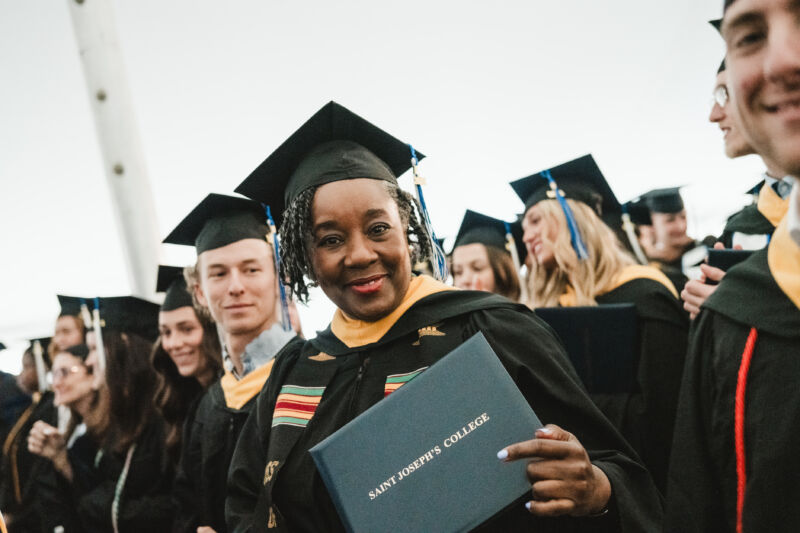 Commencement 10 Graduate holding a St. Joseph's College diploma, standing among peers in caps and gowns at the commencement ceremony. Saint Joseph's College of Maine