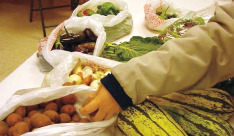 Person reaching for fresh produce on a table at Saint Joe's, including growing squashes, leafy greens, and potatoes, all placed in plastic bags. Saint Joseph's College of Maine