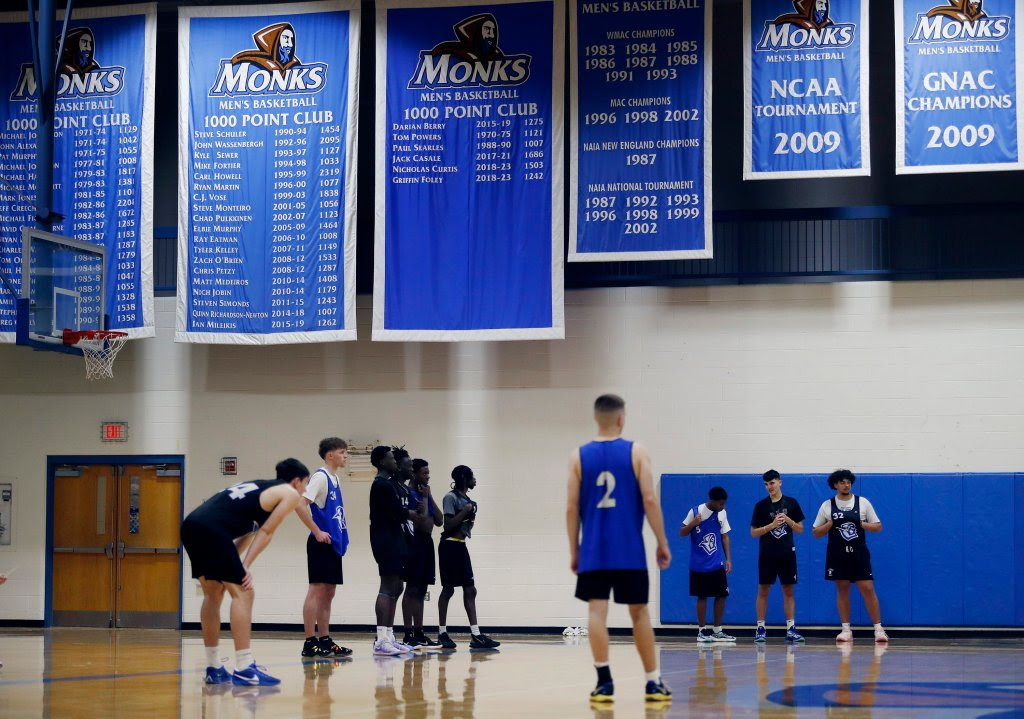 Basketball players practice on a court under blue banners displaying team achievements, including highlights from the NCAA tournament. Saint Joseph's College of Maine