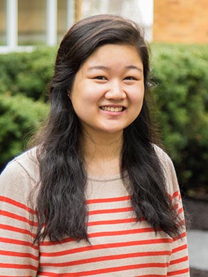 A young woman with long, dark hair wearing a beige and red striped sweater smiles outdoors with greenery in the background at Saint Joseph’s College, where she recently received the Heart and Soul Award. Saint Joseph's College of Maine