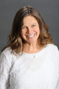 Counseling Center 2 A woman with wavy light brown hair smiles warmly at the camera. She is wearing a textured white top and a necklace with a small pendant, set against a plain gray background. Saint Joseph's College of Maine