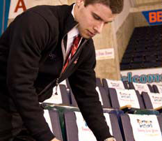 Sports Management Internships Land Students In Good Position 5 A man in a black jacket, potentially guiding students through their sports management internships, is methodically arranging items on a row of stadium seats. Saint Joseph's College of Maine