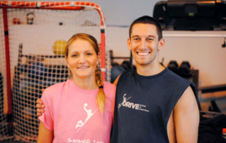 Alumni Teach Leadership On The Court In Kazakhstan 3 Two people are smiling and standing with their arms around each other in a gym. The woman, an alumni of a summer leadership program, is wearing a pink "Summer 2014" T-shirt, and the man is sporting a sleeveless shirt. A red goal net is in the background, hinting at their shared passion for sports in Kazakhstan. Saint Joseph's College of Maine