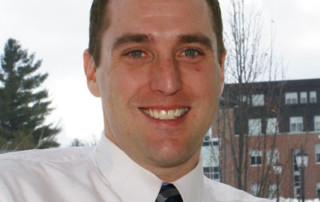 Team Leadership Guides Michael Bolanz ’00, New Director Of Alumni Relations 2 Michael Bolanz, the Director of Alumni Relations, is smiling in front of a window with trees and a building in the background, wearing a white shirt and striped tie. His friendly demeanor embodies his commitment to team leadership. Saint Joseph's College of Maine