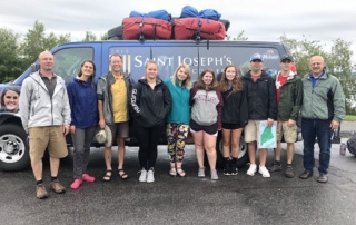 Environmental Science Semester 2018 Begins 9 A group of ten people standing in front of a van loaded with gear on the roof. The van has "Saint Joseph's" written on it. The individuals, part of the Environmental Science Semester 2018, are dressed in casual outdoor clothing. Saint Joseph's College of Maine