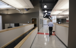 A man in a light blue shirt and dark pants is moving through an office hallway with cubicles on his left and right, as if traversing mountains of paperwork awaiting him. Saint Joseph's College of Maine