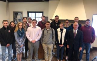 Former U.s. Assistant Secretary Of State Philip J. Crowley Speaks On Campus 2 A group of people, including ten young adults and one older man in a suit, stand indoors on campus in front of a fireplace, smiling at the camera. The older man, former U.S. Assistant Secretary of State Philip J. Crowley, stands proudly among the students. Saint Joseph's College of Maine