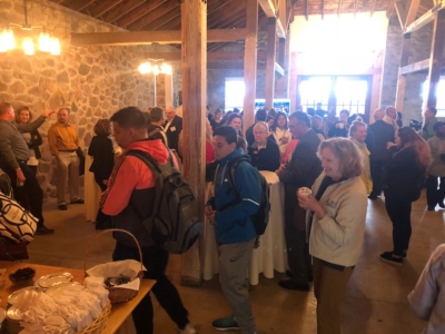 A group of people standing and interacting in a rustic, indoor event space with wooden beams and stone walls, at a 911 Commemorative Event hosted by Saint Joseph’s College, some holding drinks and snacks. Saint Joseph's College of Maine
