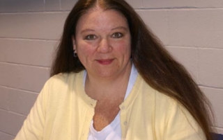 New Major In Special Education To Begin Next Fall 7 A woman with long brown hair, wearing a yellow cardigan and a white shirt, is sitting against a light-colored brick wall, looking into the camera. Her thoughtful expression suggests she's contemplating a new major in special education. Saint Joseph's College of Maine