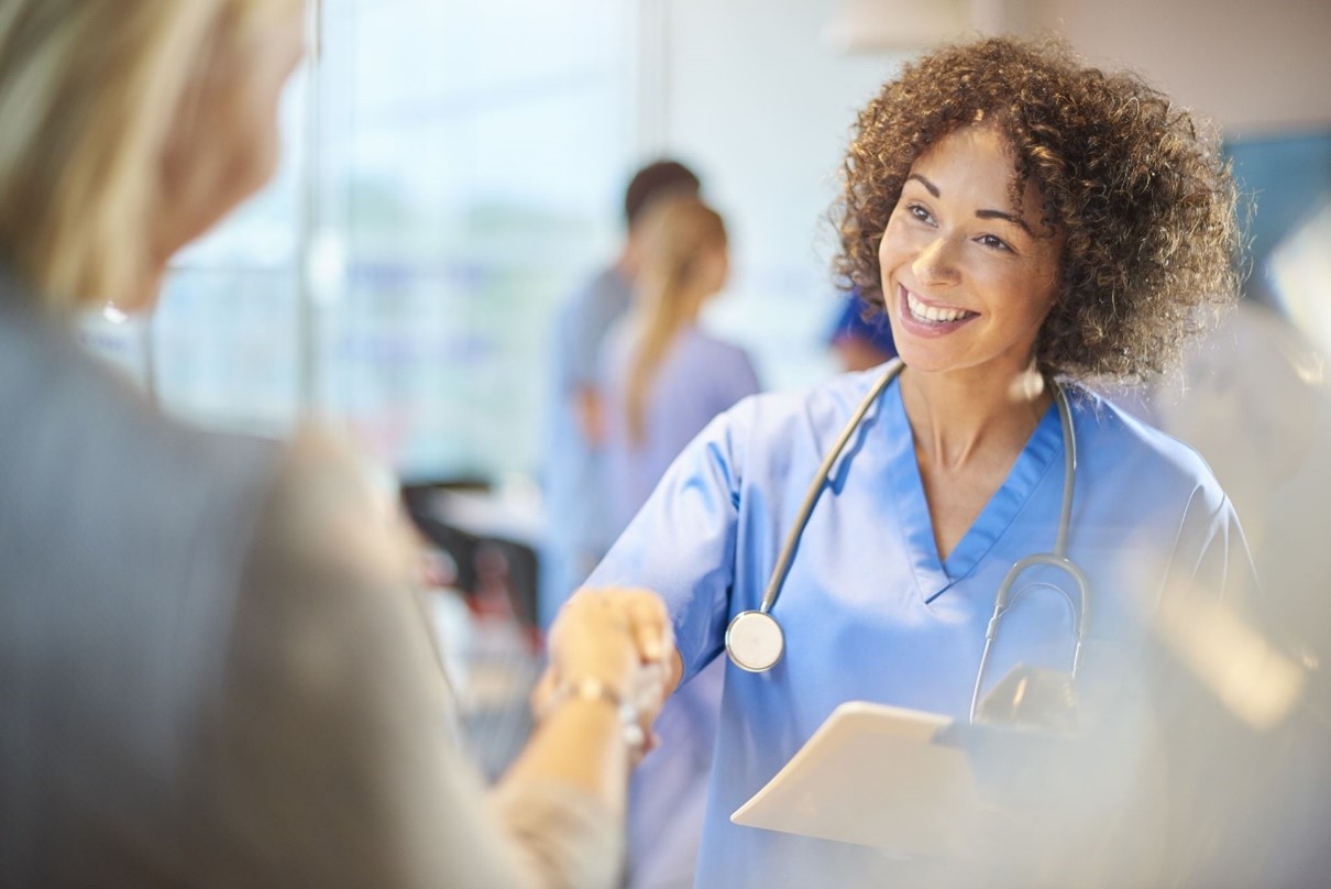 Nurse With Clipboard A medical professional in blue scrubs and a stethoscope smiles and shakes hands with a person, while holding a clipboard. Saint Joseph's College of Maine