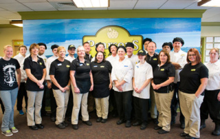 Food Service Gets A Whole Lot More Local 2 A group of people in uniform stand together posing for a photo inside a building with a sign that reads "Paragon's" in the background, showcasing their local food service unity. Saint Joseph's College of Maine