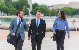 A Summer On Capitol Hill: Raymond Mosca ‘19 Interns For Congressman Bruce Poliquin 9 Three people in professional attire walk and talk outdoors near a body of water in an urban park setting, giving the scene a vibe reminiscent of Summer on Capitol Hill. Saint Joseph's College of Maine