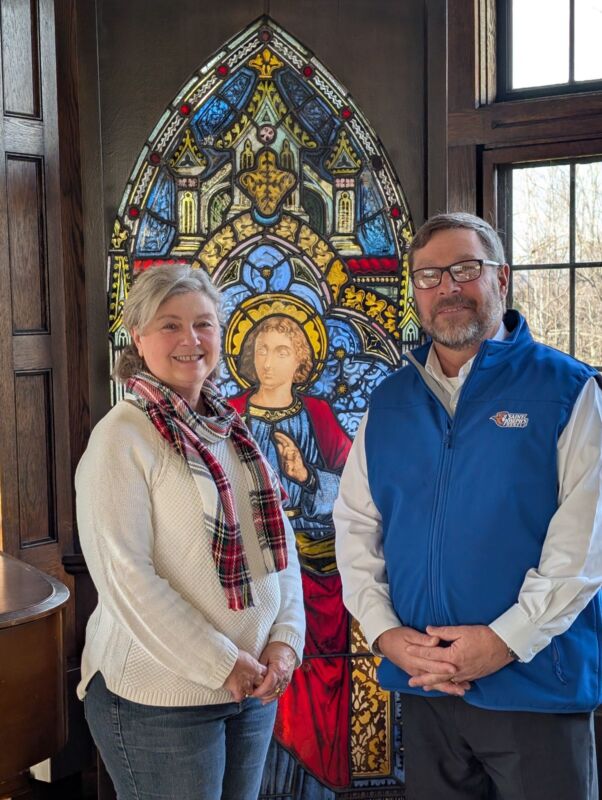Sjc Gets $100K For Simone Blanchette Nursing Scholarship 1 Two people standing in front of a decorative stained glass window featuring a religious figure at Saint Joseph’s College of Maine, capturing the spirit and dedication of nursing students. Saint Joseph's College of Maine