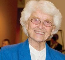 Sister Mary George O’toole Switches Roles 5 Sister Mary George O'Toole, an elderly woman with white hair and glasses wearing a blue blazer and white shirt, smiles at the camera. Saint Joseph's College of Maine
