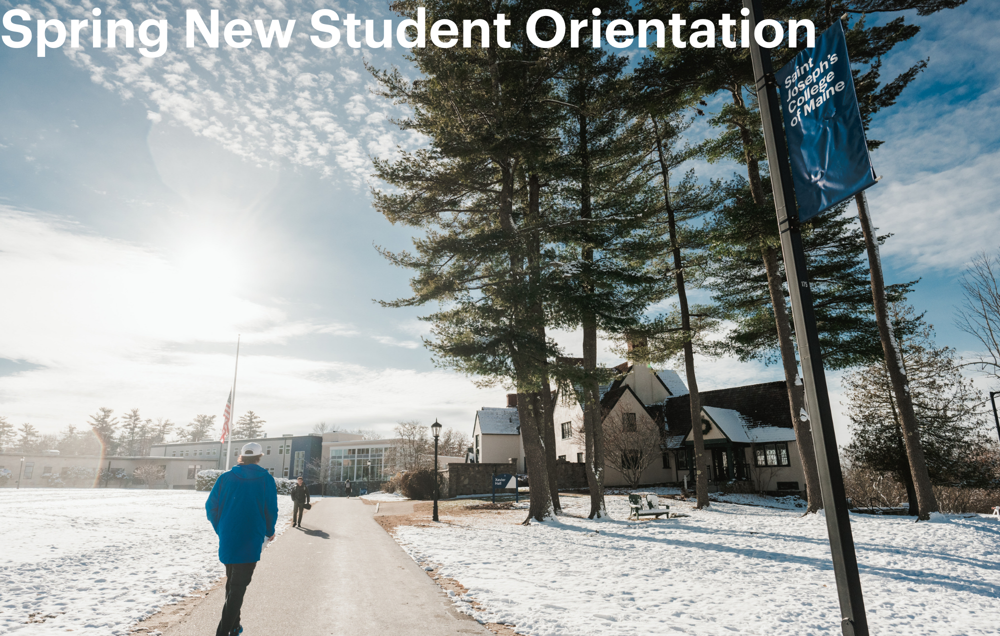 People walk along a snowy campus path under a clear sky, heading to a building for new student orientation, as a banner reading “Spring New Student Orientation” is displayed in the background. Saint Joseph's College of Maine