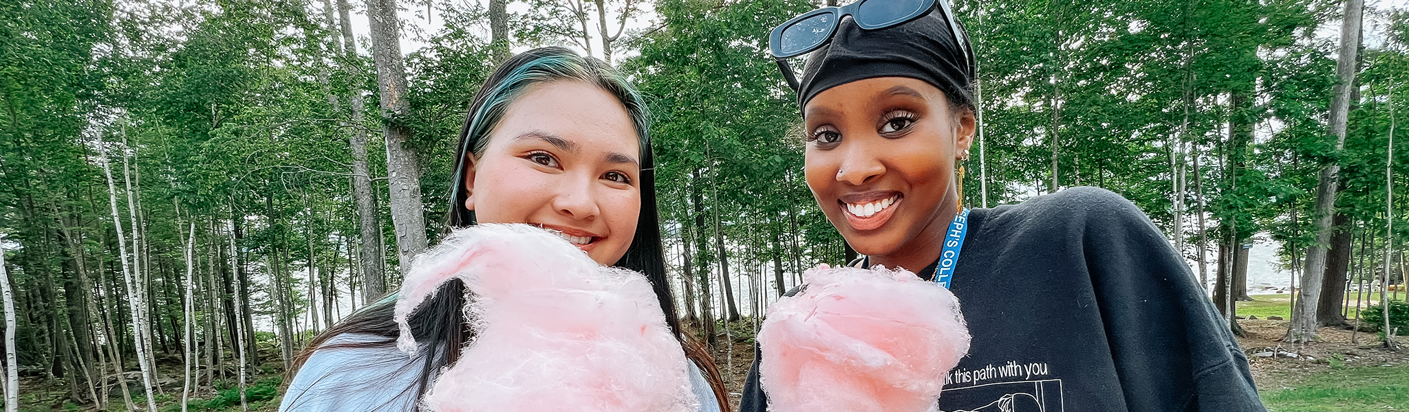 Talbots Two people smiling and holding pink cotton candy in an outdoor setting with trees in the background, embodying a sense of joy that reflects the spirit of justice, equity, diversity, and inclusion. Saint Joseph's College of Maine
