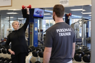 Return On Investment 2 Tommy looks on as Mary Lynn lifts an exercise weight over her head