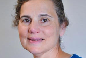 College Names New Online Theology Director And Certificate Programs 8 A woman with short, curly brown hair, wearing a blue top, smiles while looking at the camera against a plain background. As an Online Theology Director for her college's certificate programs, she exudes confidence and warmth. Saint Joseph's College of Maine
