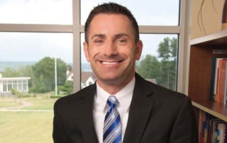 Meet Vincent J. Kloskowski Iii ’95 8 A man in a suit and striped tie is smiling, standing in front of a window with a scenic outdoor view. There is a bookshelf on the right side of the image, adorned with various books. You might recognize him as Vincent J. Kloskowski III, class of '95. Saint Joseph's College of Maine