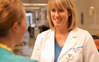 Saint Joseph'S College Of Maine Announces Online Bsn Tuition Rate For Eligible Maine Community College Students 2 A nurse in a white coat with an RN badge chats with a colleague in green scrubs in a hospital hallway, perhaps discussing the radical notion of extending their lunch break. Saint Joseph's College of Maine