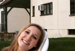 The Campbell Women 1 A person with light hair and a white shirt is reclining on a lounge chair outdoors in front of a building with air conditioners in the windows, reminiscent of the tranquil moments often enjoyed by the Campbell Family. Saint Joseph's College of Maine