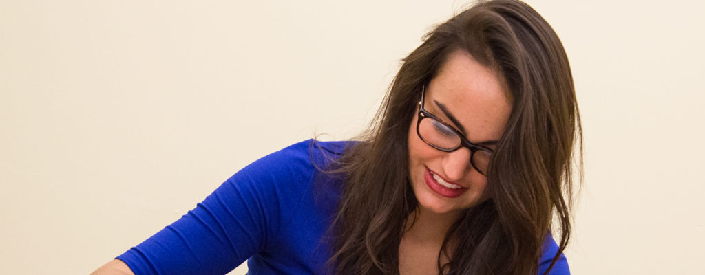 A woman with long brown hair and glasses, wearing a blue shirt, is looking down and smiling as she discusses various campus programs. Saint Joseph's College of Maine