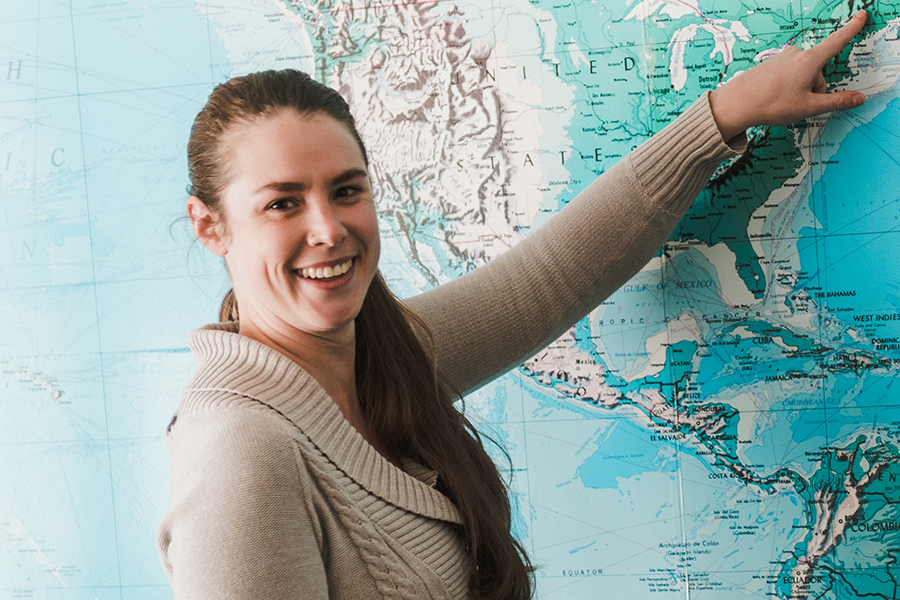 G-Education A woman with a ponytail, smiling and pointing to a location in the northeastern United States, stands in front of a large map. She is eager to share that this area hosts an esteemed graduate program available both on-campus and as an online program. Saint Joseph's College of Maine