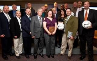 Athletics Hall Of Fame 2012 4 A group of people, dressed in formal and business attire, are standing together in a room. Two individuals in the front row are holding basketballs, likely honored for their athletics achievements with a Hall of Fame induction in 2012. Saint Joseph's College of Maine