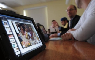 Ipads, Skype And Apple Tv = International Management Class 8 A group of people sit at a conference table with iPads in front of them, one showing a presentation with an image of a child. Saint Joseph's College of Maine