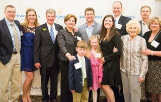 Shea Family Ties 9 A group of adults and two children are standing and smiling in front of a Saint Joseph's College banner at an event, celebrating the strong Shea Family Ties. Saint Joseph's College of Maine