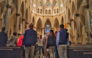 Holy Year Of Mercy Pilgrimage 3 A group of people on a pilgrimage stand inside a large church with high arched ceilings and stained glass windows, marking the Holy Year of Mercy. Saint Joseph's College of Maine