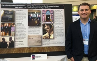 Statewide Education Consortium Launches North Atlantic And Arctic Showcase 5 A person stands beside a display titled "Curating Governor Brennan’s Legacy: My Semester at the Brennan Archives," featuring various photos and text panels. As part of the Statewide Education Consortium, the person holds a certificate while smiling at the camera, celebrating their achievement. Saint Joseph's College of Maine
