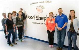 Saint Joseph’s Day Of Service 4 A group of people from Saint Joseph stand smiling in front of a sign that reads "Good Shepherd Food Bank of Maine" with the tagline "Partnering to End Hunger" during their Day of Service. Saint Joseph's College of Maine