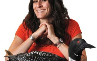 People Love Loons 1 A woman with long dark hair, wearing a red shirt, smiles and sits behind a taxidermy loon on a nest—a scene that captures why people love loons. Saint Joseph's College of Maine